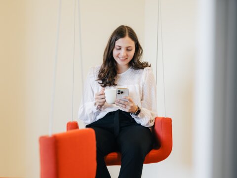 Employee enjoys her break with coffee and Iphone on the office swing. | © instride AG