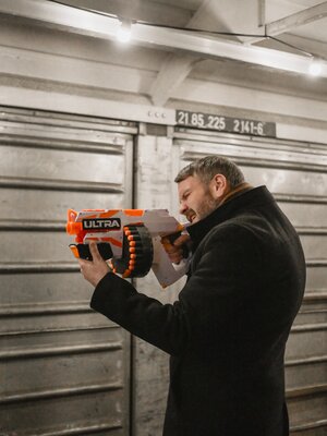 Employee holds a Nurf gun in his hand and aims at the cans.