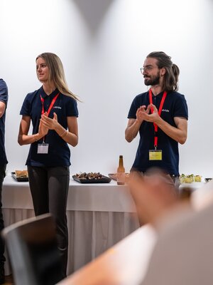 Eine Frau und zwei Männer stehen vor dem Publikum und sprechen beim BeerTalk.